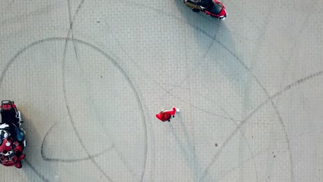 red-haired woman standing in the centre of two professional motorcyclists riding around her. top view of a beautiful young female and motorbikers on the road.