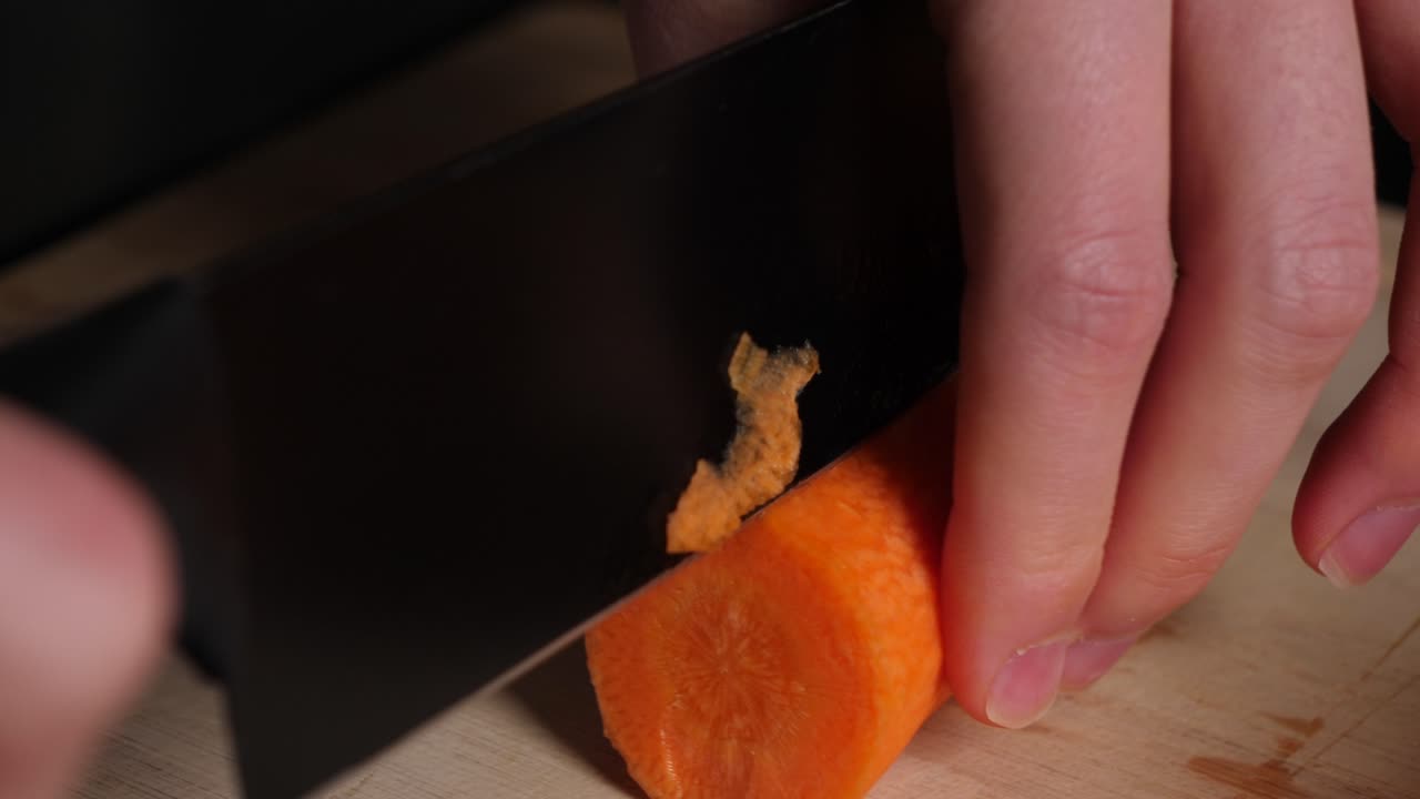 las manos del chef cortan las zanahorias en pedazos por la mitad en la tabla de cortar madera