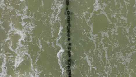 Luftaufnahme-Der-Ostseeküste-Aus-Der-Vogelperspektive-An-Einem-Bewölkten-Tag,-Alter-Holzsteg,-Weißer-Sandstrand,-Große-Sturmwellen,-Die-Gegen-Die-Küste-Schlagen,-Klimawandel,-Weit-Aufsteigende-Drohnenaufnahme