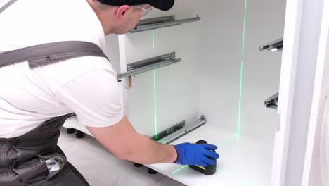 a young craftsman in a black cap uses an electronic level to install kitchen furniture