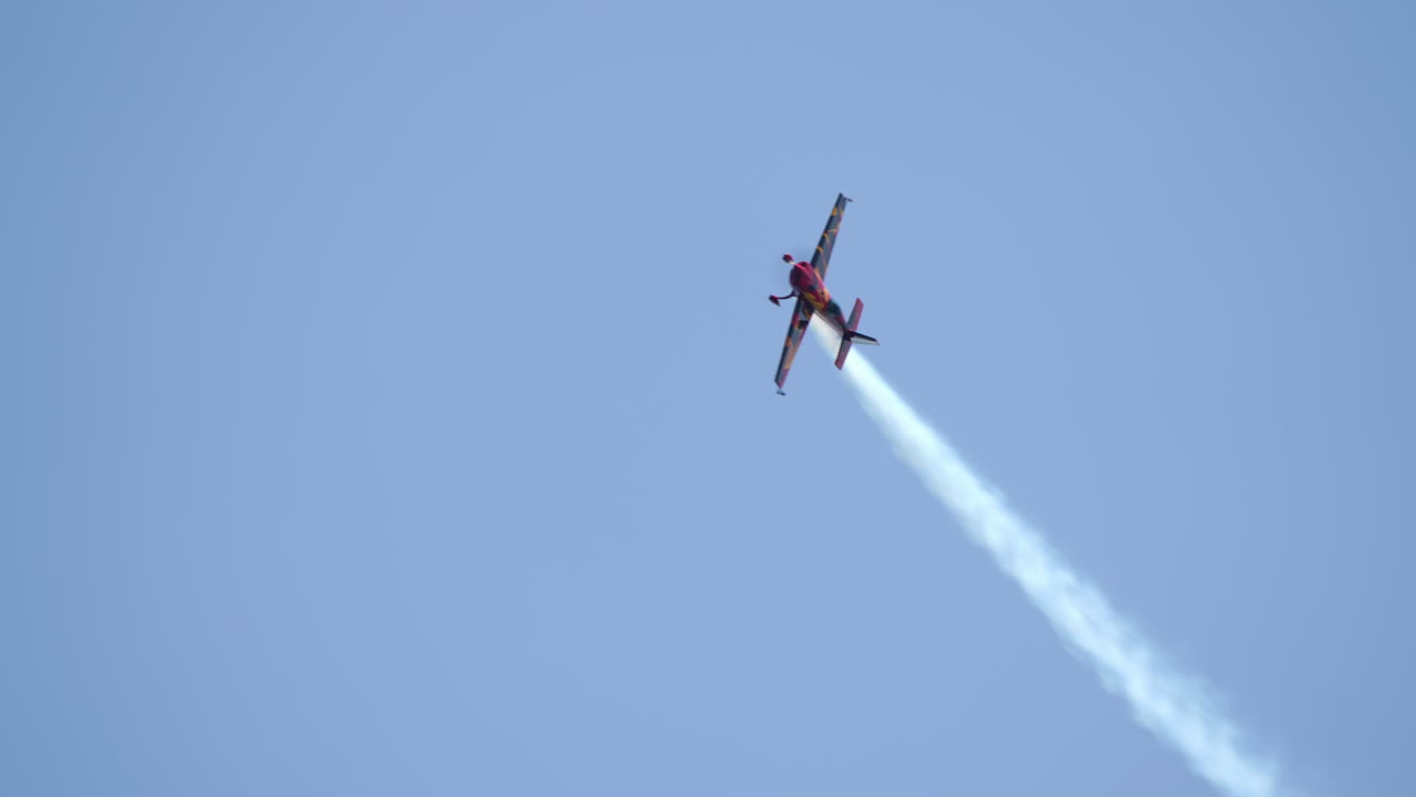 Small airplane performing stunt with white smoke trail during flight at airshow under blue sky