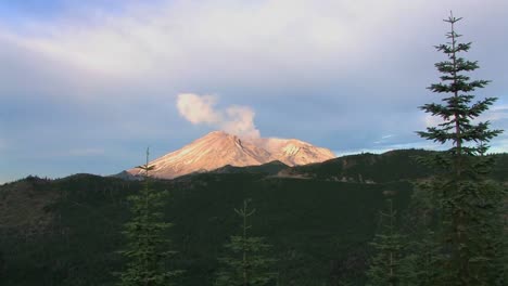 the collapsed caldera of mount st helen's smokes above the forested hills of the national park