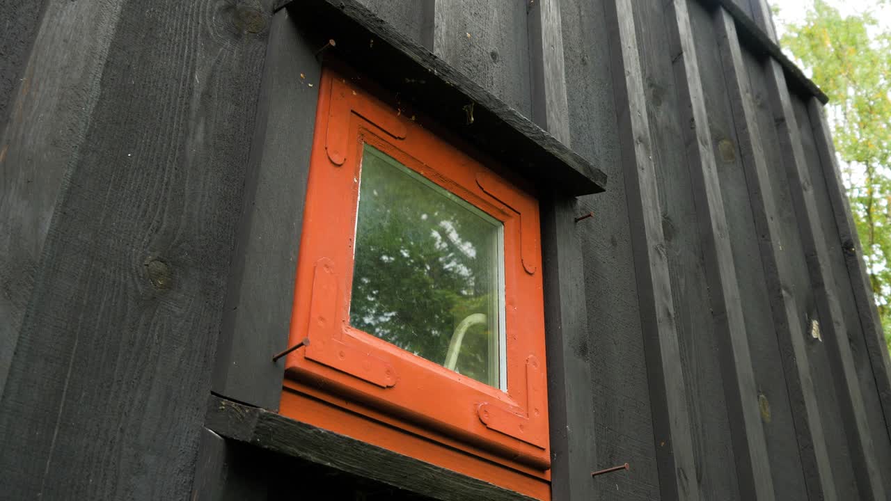 Utvendig utsikt over et svartmalt, gammelt, tradisjonelt trehus, lite rødt vindu, overskyet dag, medium håndholdt opptak.