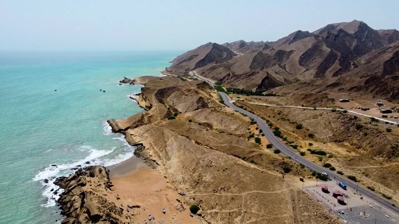 Un video drone cattura ampie riprese aeree delle montagne rocciose di Kund Malir, della costa turchese e di un'area di sosta lungo la strada sotto la luce del giorno in Balochistan, Pakistan. Nessuna persona visibile