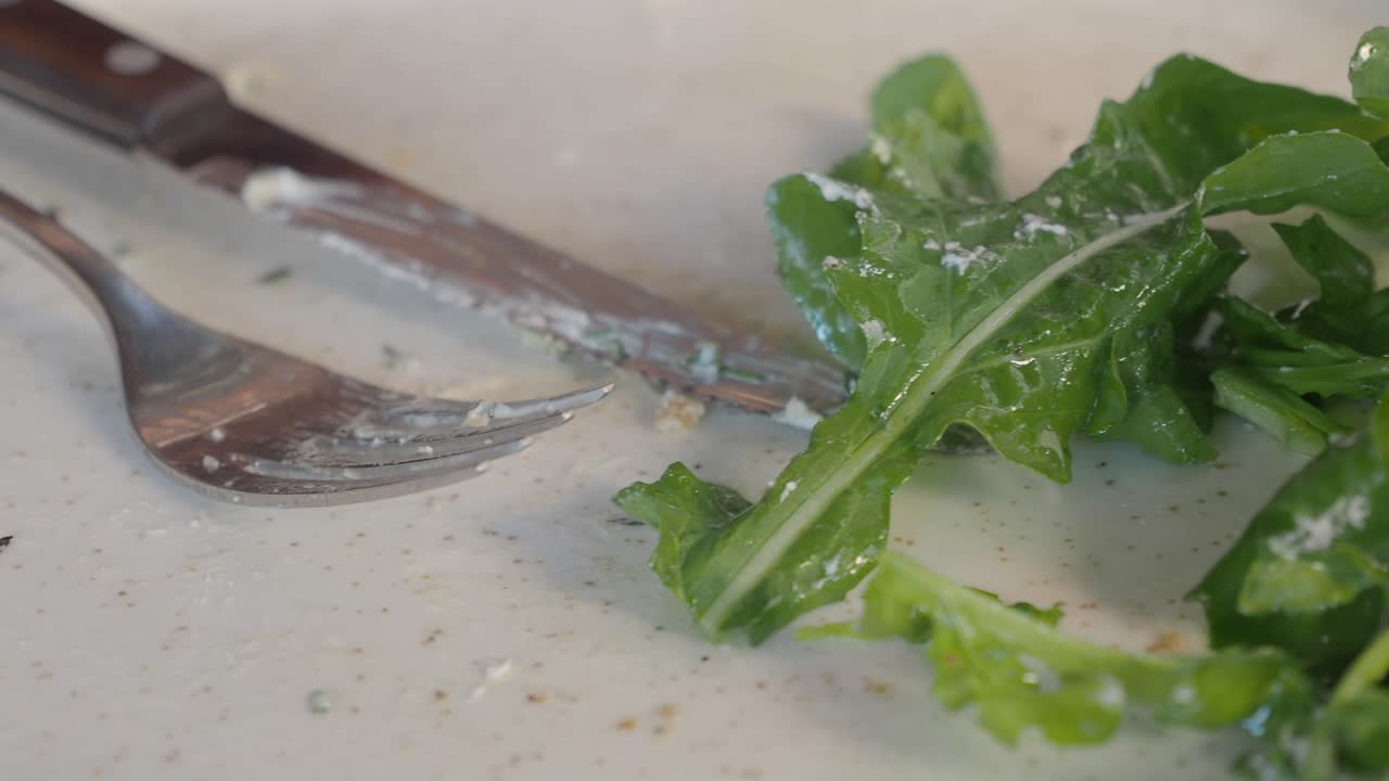 Leftover arugula and cutlery on a dirty plate