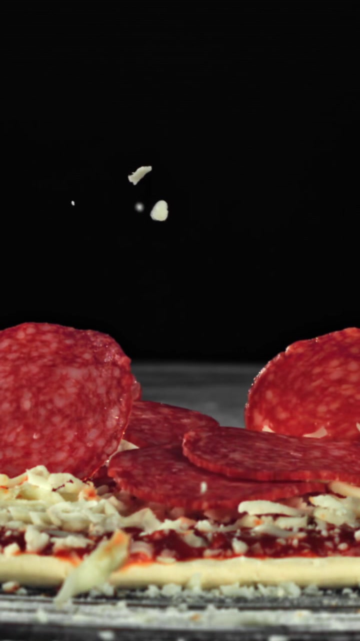 Al rallentatore: salame piccante e formaggio che cadono su pizza cruda