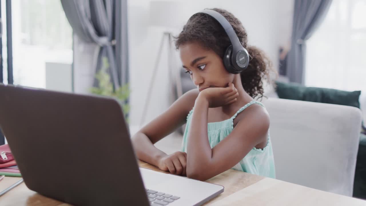 chica afroamericana sentada en una mesa, usando una computadora portátil para una lección en línea, cámara lenta