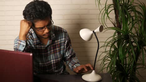 young man studying at desk with laptop and lamp