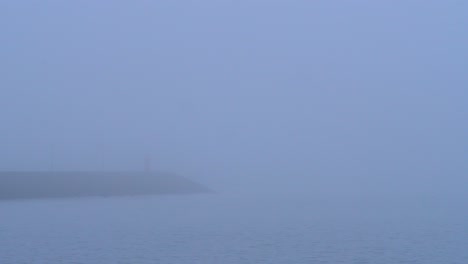 fog over sea and seaside town at sunrise with calm water and colourful sky