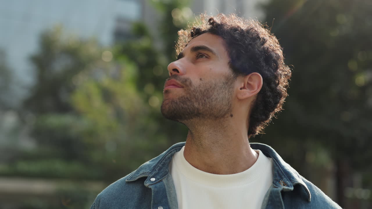 Young Man with Curly Hair Looking Up and Smiling Outdoors