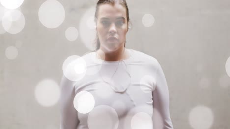 animación de manchas de luz sobre tamaño plus mujer caucásica en ropa deportiva flexionando los músculos