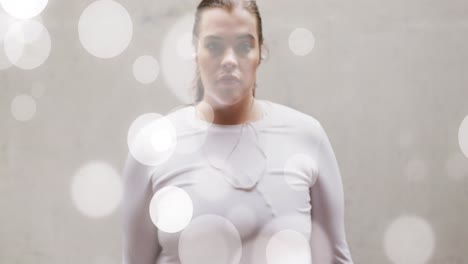 animation of spots of light over plus size caucasian woman in sports clothes flexing muscles