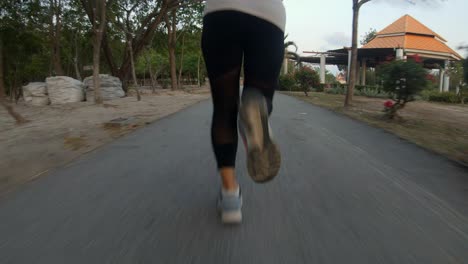 a slowmotion follow up shot of a young thai girl jogging in a local park , the shot is focused on her legs as she runs forward