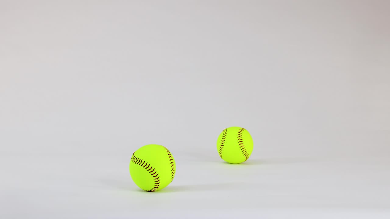 Due softball giallo neon che rimbalzano e atterrano su sfondo bianco