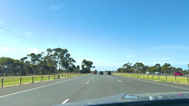 A scenic drive on Great Ocean Road with clear skies, lush greenery, and smooth asphalt, captured in bright daylight