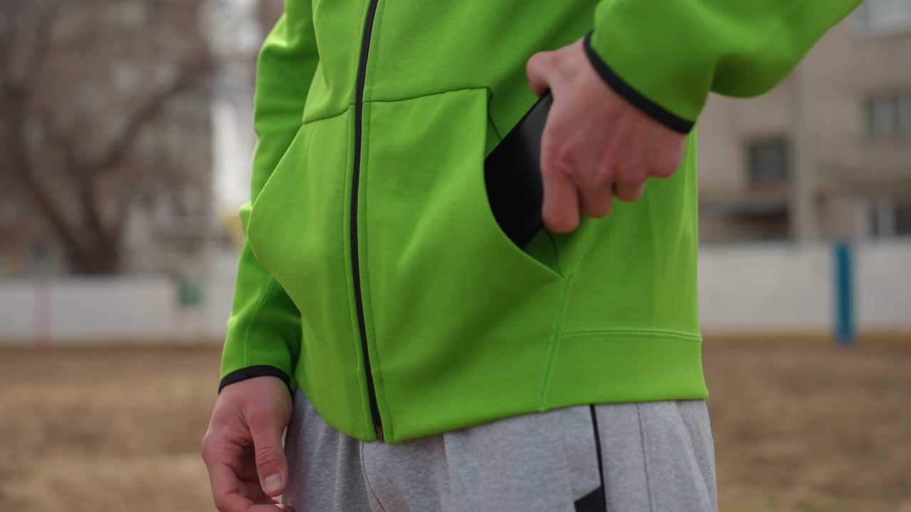 편안한 야외 키 조정, 평화로운 도시 공원 환경에서 키를 조정하는 손의 클로즈업, 녹색 재킷 주머니에서 키를 편안하게 조정하는 손을 클로즈업하여 보여주는 도시 공원 장면