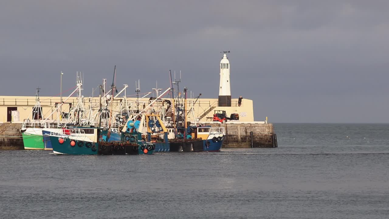 A fishing boat entering harbour with other vessels moored to the harbour wall. Peel. Isle of Man. UK. Winter