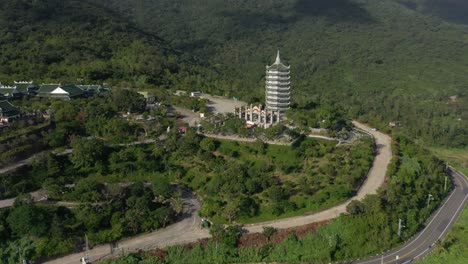 Aerial-circling-around-tall-Lady-Buddha-statue-and-temple-tower-with-huge-mountains-and-ocean-in-Da-Nang,-Vietnam