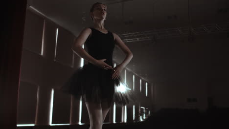 graceful woman ballerina in a dark dress on a dark stage of the theater in the smoke performs dance moves in slow motion.