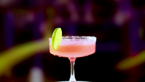 a pink margarita cocktail is poured into a glass with a lime garnish, set against a colorful background