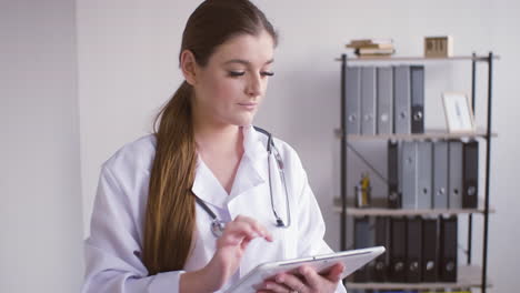 Redhead-doctor-woman-in-white-coat-using-a-tablet-and-looking-at-the-camera