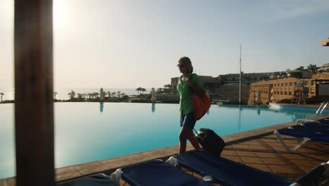 steadicam shot of woman with travel bag walking on recreation area along the pool