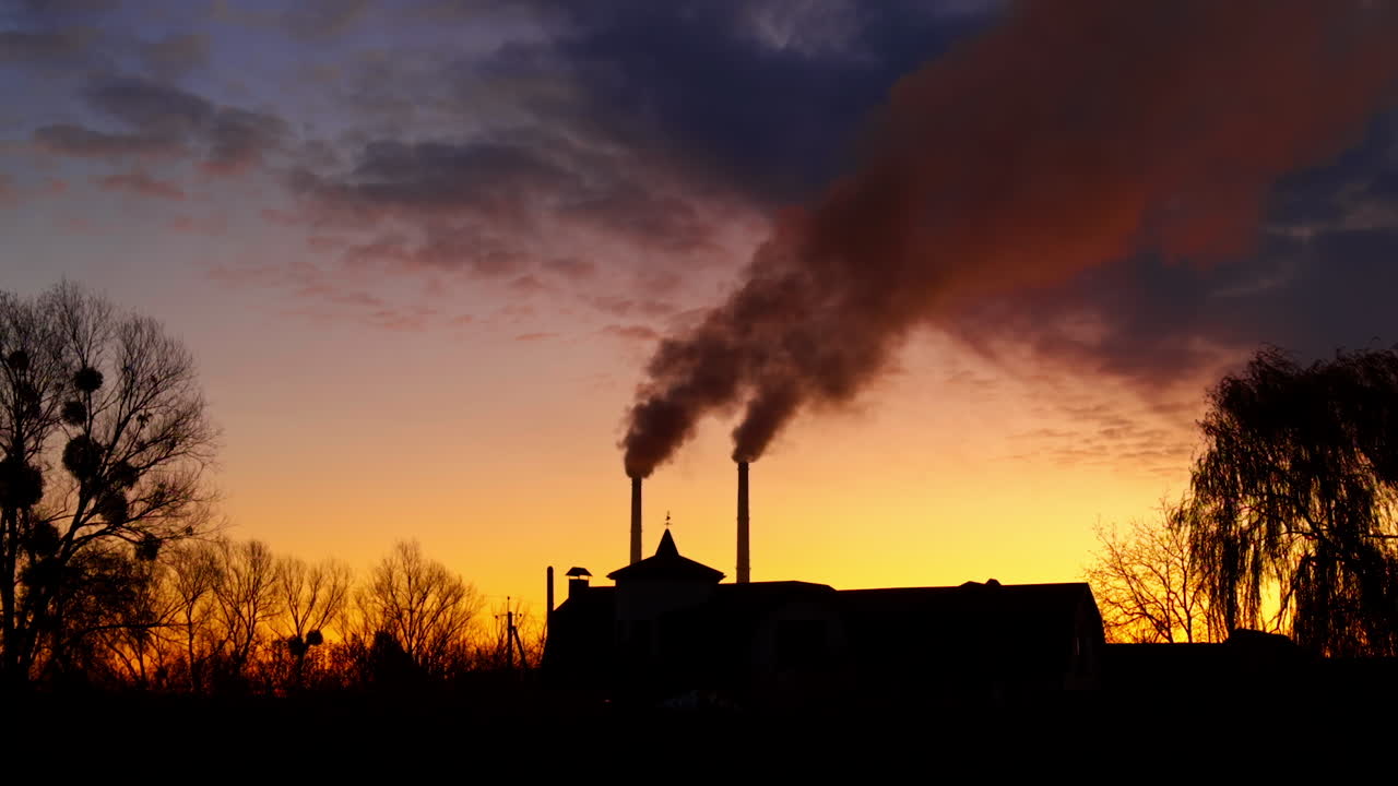 Two pipes rising above the building. Heavy dark smoke gathering in the atmosphere. Sunset landscape.