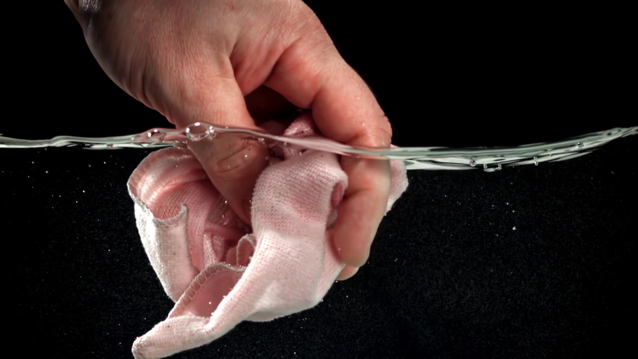Mano che stringe un panno rosa nell'acqua al rallentatore