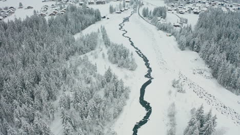 Drone-Siguiendo-El-Río-Y-Revelando-La-Hermosa-Ciudad-Suiza-En-Un-Paisaje-Cubierto-De-Nieve