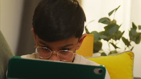 close up of young boy sitting on sofa at home playing games or streaming onto digital tablet 2