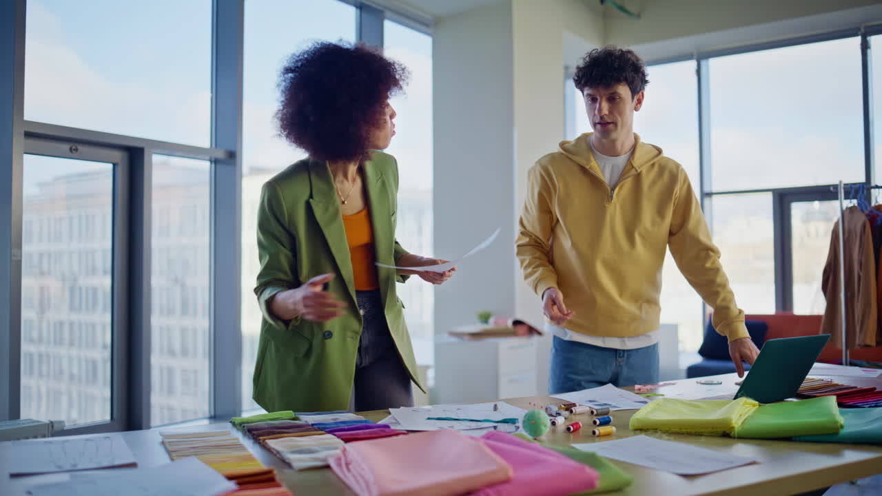Creative designers selecting fabric with sketches in light office. Two tailors