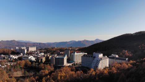 Slow-moving-aerial-pan-over-beautiful-town-in-mountains-during-autumn-colors-on-bright-day