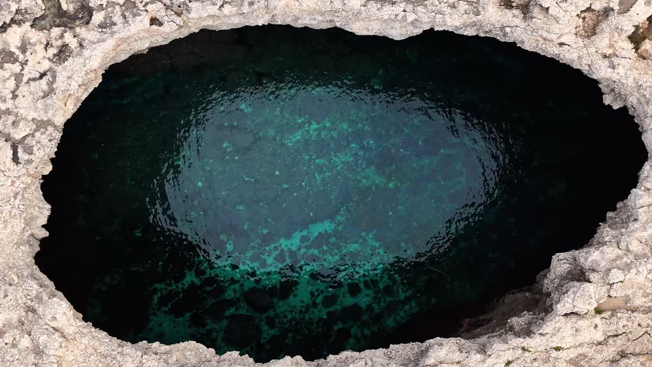 Uma perspectiva aérea de cima para baixo captura a vibrante água turquesa dentro da formação rochosa natural de calcário da Lagoa de Coral em Mellieha, Malta.