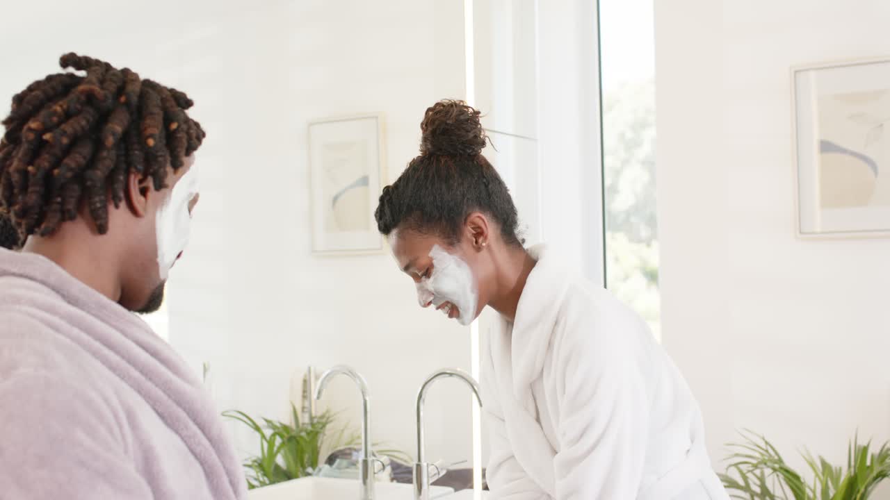 African American couple at bathroom sink, woman turning faucet rinsing mask off, man watching