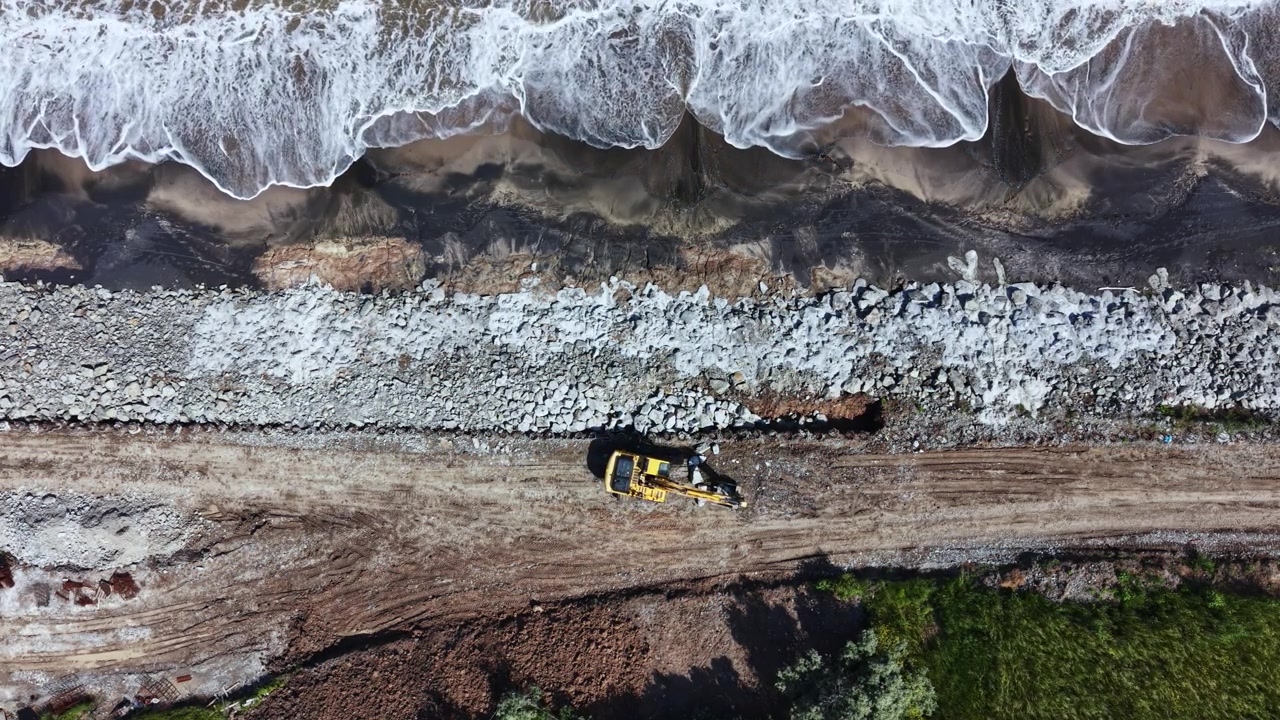 Lavori di costruzione lungo la costa con macchinari pesanti che movimentano materiali vicino all'acqua di giorno