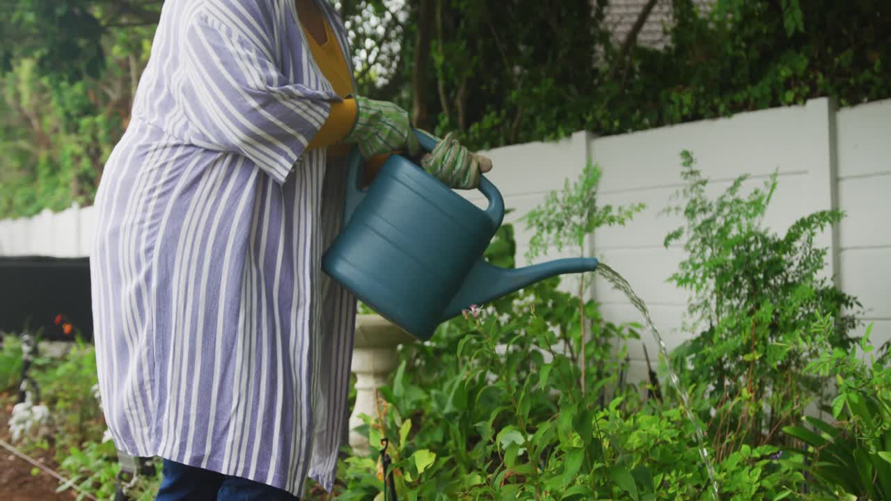 video de una feliz mujer afroamericana de tamaño grande regando flores en el jardín
