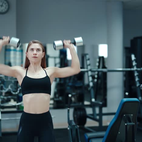 slim woman in a black top and leggings performs an exercise with her hands with dumbbells in the gym. sport equipment. blurred background