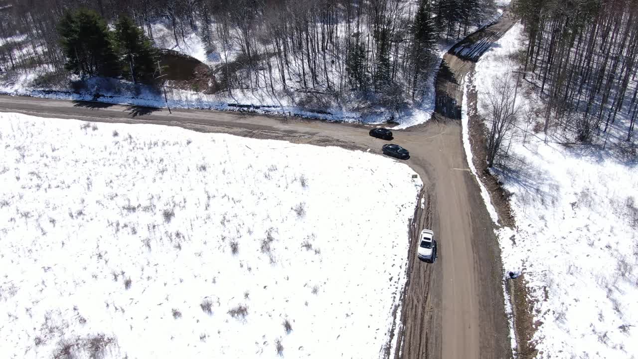 imágenes aéreas de drones siguiendo a un camión negro conduciendo por un camino de tierra en un bosque cubierto de nieve