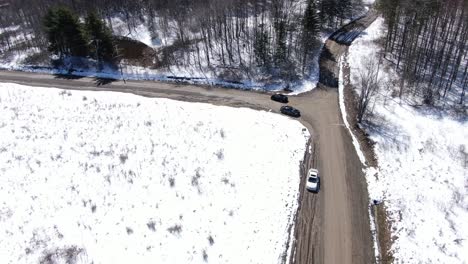 一架黑色的汽车在雪覆盖的森林里沿着一条土路行驶的空中无人机录像