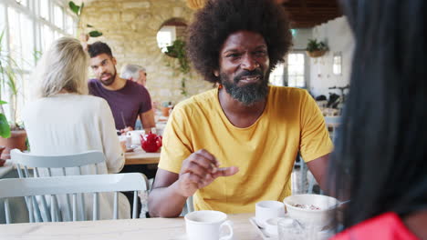 Middle-aged-black-man-eating-breakfast-and-drinking-coffee-with-his-girlfriend-at-a-restaurant,-seen-over-her-shoulder,-close-up