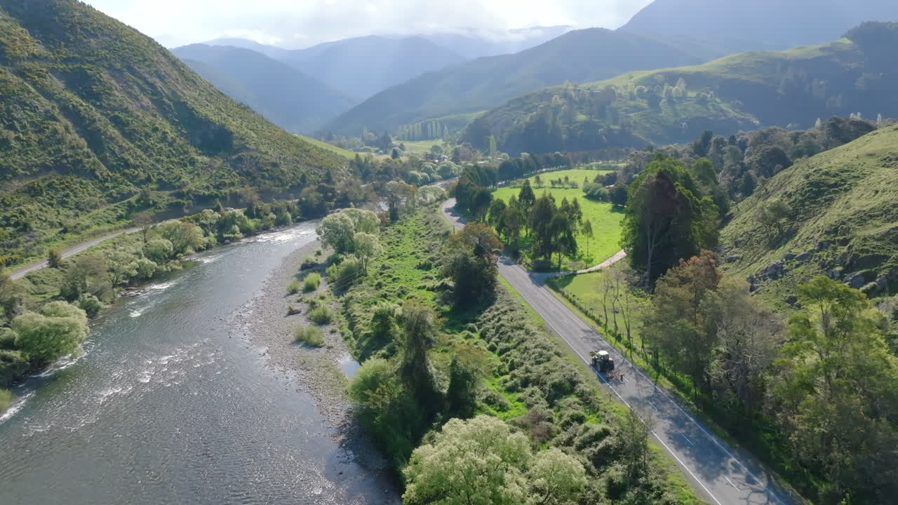 un avión no tripulado de un tractor conduciendo a lo largo del río motueka pasando por campos verdes y exuberantes en un día soleado en nueva zelanda