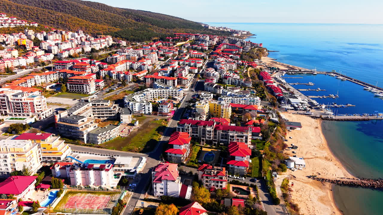 Oteller, yüzme havuzları, kumlu bir plaj ve yat marinası içeren bir sahil tatil köyünün gündüz havadan görünümü. Kıyı kasabası mimarisi.