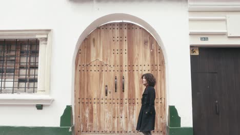 A-woman-in-a-suit-with-curly-hair-walks-in-front-of-an-old-building-in-the-city-of-Bogota,-Colombia