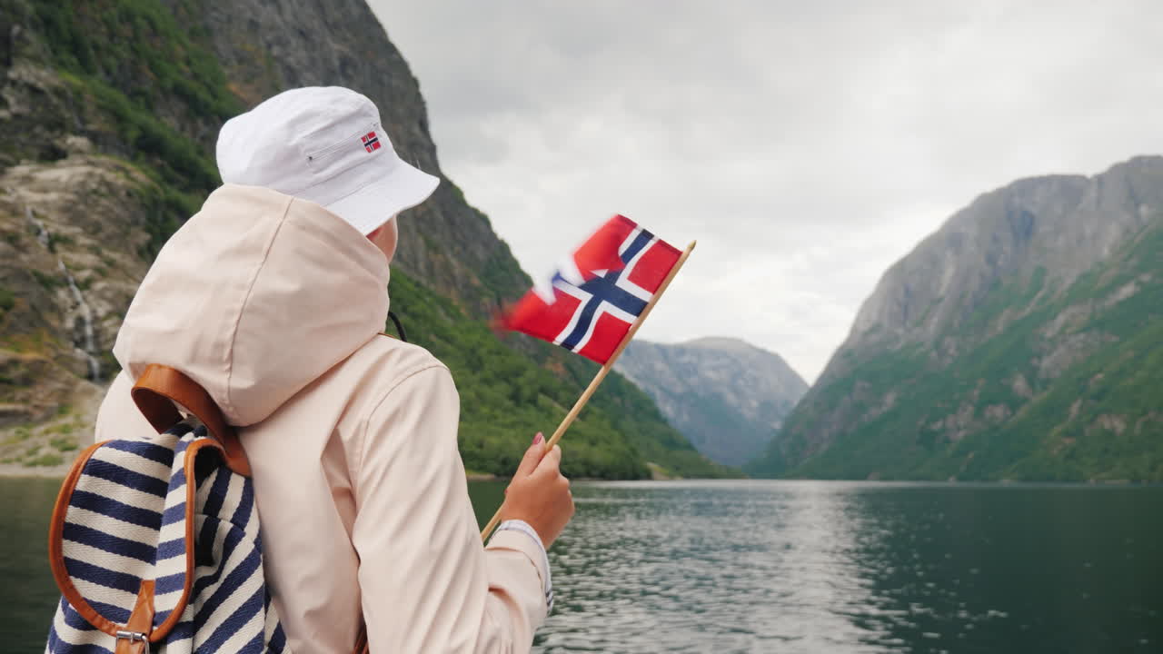 En turist med norsk flagg står på baugen av et cruiseskip Reise gjennom det pittoreske