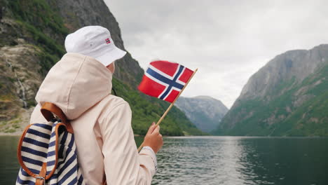 un turista con una bandera de noruega se encuentra en la nariz de un viaje en crucero por el pintoresco