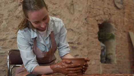 woman potter working on potter wheel making a clay pot. master forming the clay with her hands creating pot in a workshop