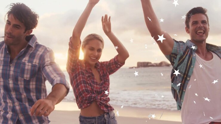 Trio che cammina e balla sulla spiaggia al tramonto, le risate creano un effetto di stelle che si muovono sopra di loro, con le braccia alzate, per marketing.