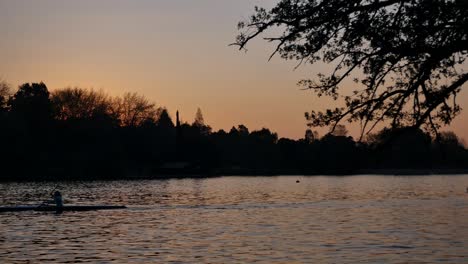 Silueta-De-Mujer-Remando-En-Canoa-En-Reluciente-Presa-Al-Atardecer,-Hora-Dorada