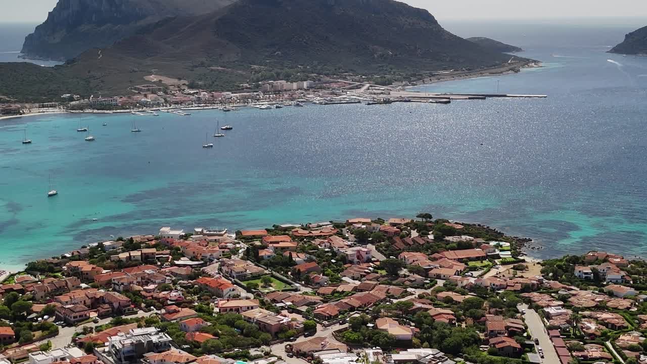 Vista di una città costiera in Sardegna con barche e montagne in lontananza
