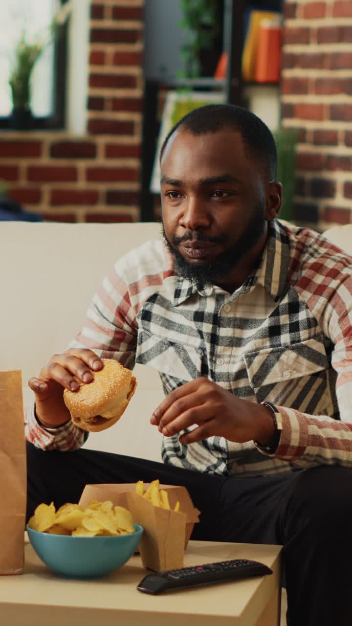 Vertical video: African american guy having fun eating burgers